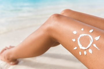 Sunscreen sun drawing lotion on suntan legs relaxing tanning on tropical beach holiday.
