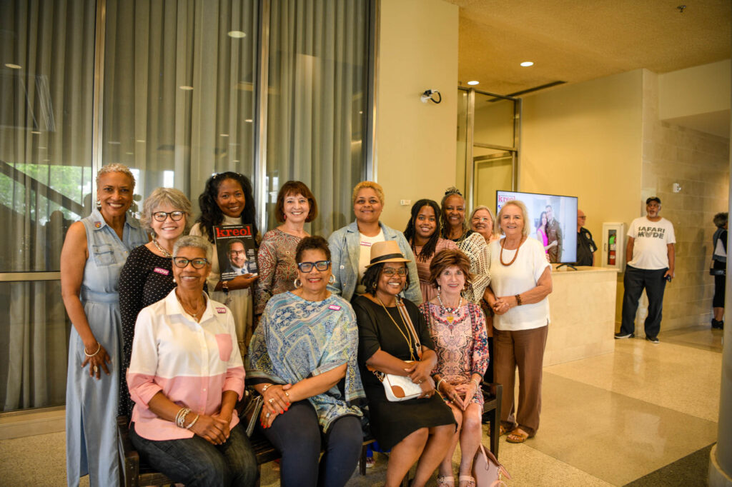 _D856446 - International Magazine Kreol Group of smiling women posing together in a bright lobby, some seated on a bench and others standing behind them.