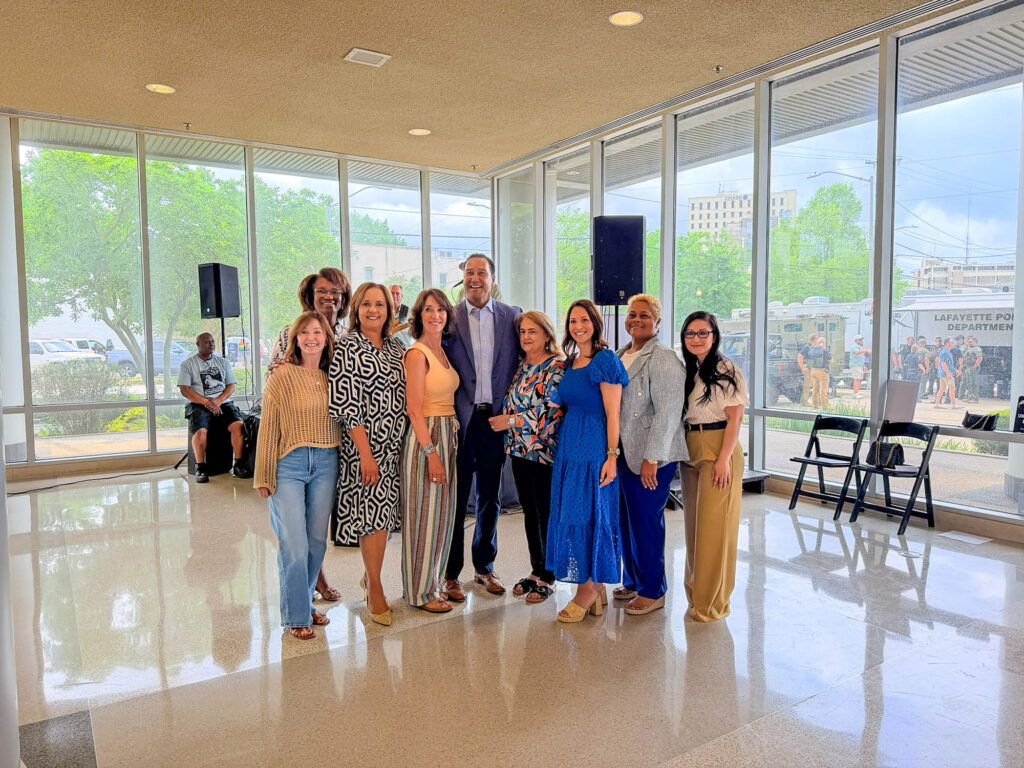IMG_2888 - International Magazine Kreol Group of adults posing together indoors in a bright lobby with large windows and a reflective tile floor, some smiling for the camera.