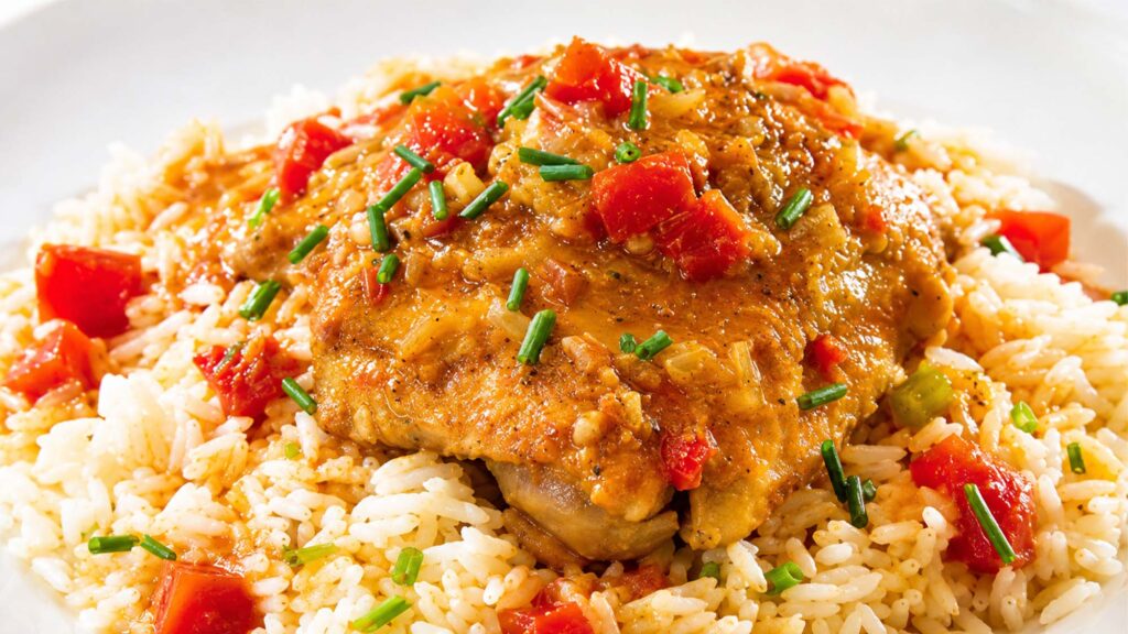 Pork chop resting on a bed of seasoned rice with red peppers, garnished with chopped chives.