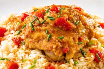 Pork chop resting on a bed of seasoned rice with red peppers, garnished with chopped chives.