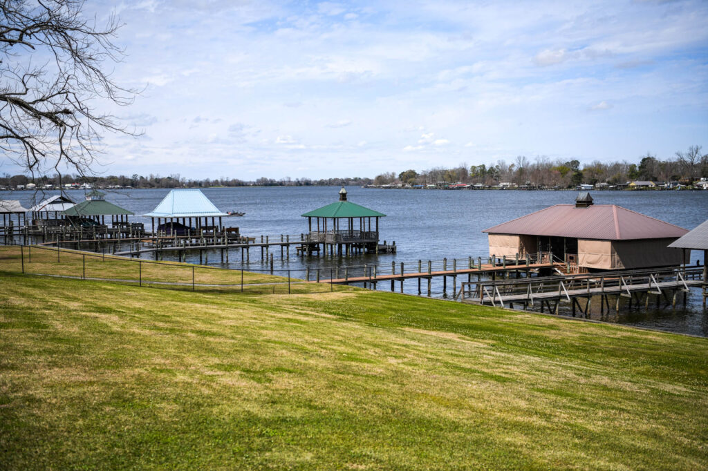 _D851604 - International Magazine Kreol Lakeside scene with wooden piers and colorful gazebo overlooks on calm water, grassy foreground and leafless tree branches on the left.