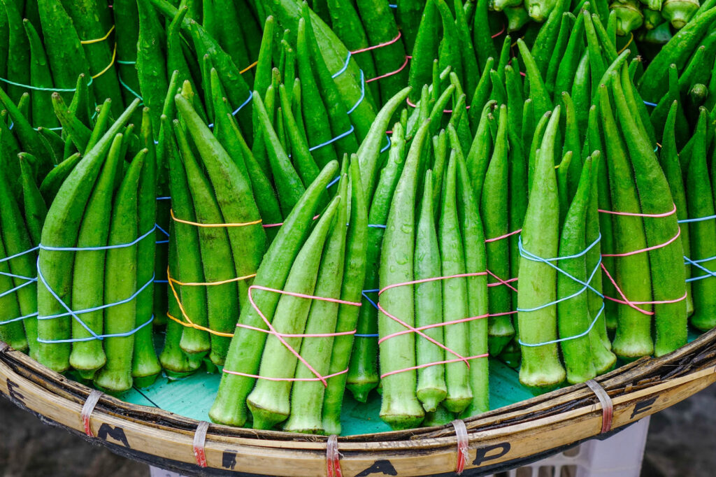 GreenOkraAtTheFarmerMarketInManilaPhilippines - International Magazine Kreol Bundles of fresh long green beans tied with colorful strings in a woven basket.