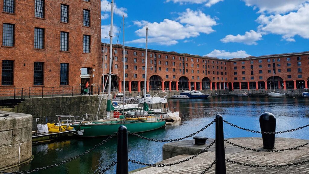 Port - International Magazine Kreol Red brick warehouse complex along a marina, with moored sailboats and a blue sky.