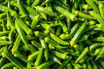 Bundles of fresh long green beans tied with colorful strings in a woven basket.